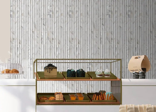 Estudio Cerámico Argos 'Calacatta Gold', witgrijze marmerlook wandtegels met verticaal reliëf achter een vitrine met gebak