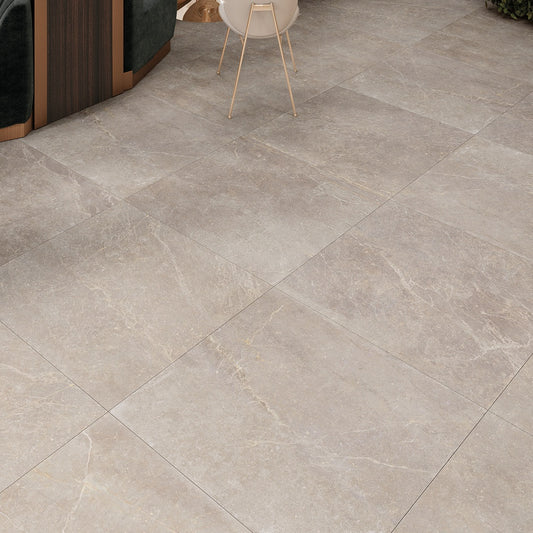 Keraben Bleuemix 'Taupe Soft', taupe vloertegels in groot formaat van dichtbij, met een stoel en groen op de achtergrond