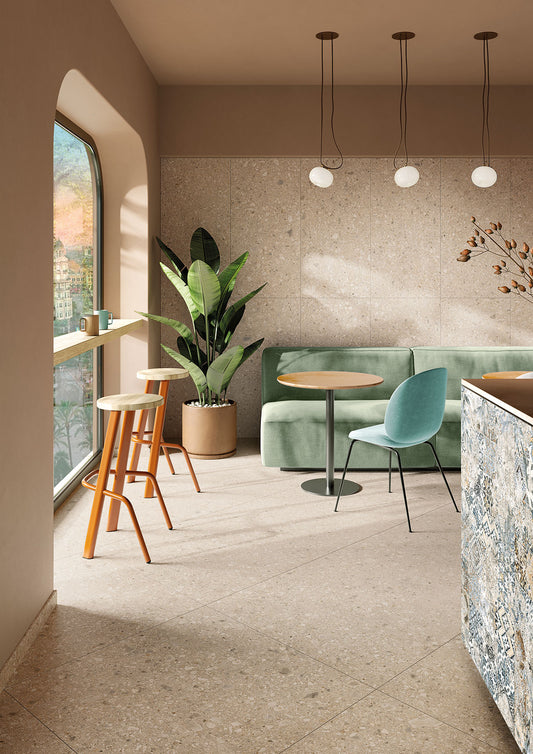Tuscania Ceppo di Gré 'Beige', beige terrazzo vloer- en wandtegels in een koffiebar met groene bank en witte bollampen