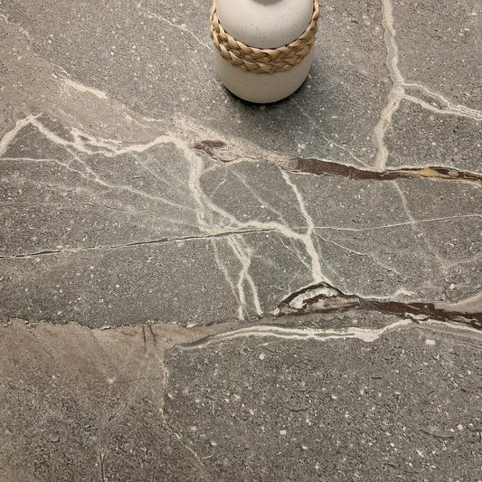 La Platera Dusk 'Taupe', detail van taupe marmerlook tegel 60x60cm met witte aders en een vaas