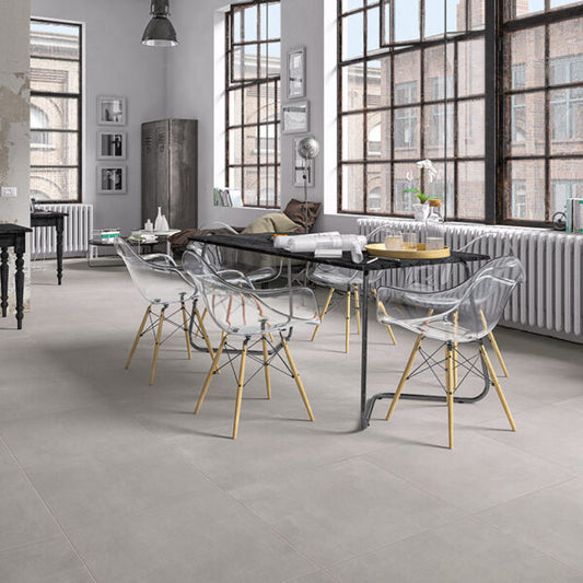 Ceramica Valsecchia Galaxy 'Grey', lichtgrijze betonlook vloertegels in een loft met lange eettafel en transparante stoelen