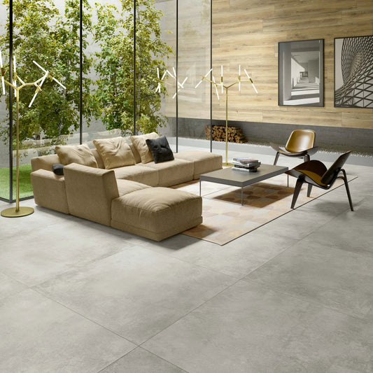 EnergieKer Parker 'Silver', lichtgrijze betonlook vloertegels 120x120cm in een woonkamer met beige hoekbank en binnentuin