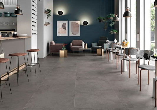Ceramica Valsecchia Recover 'Dark', grijze betonlook vloertegels in een loungeruimte met donkerblauwe wand en fauteuils