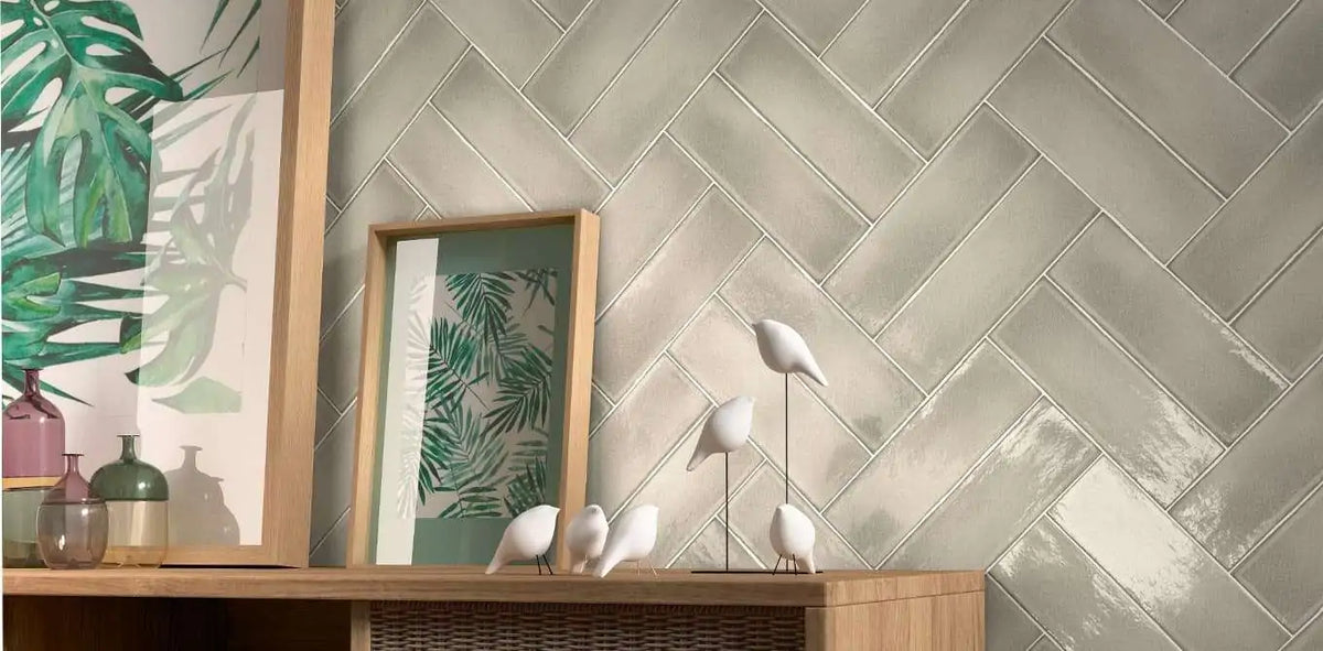 Estudio Cerámico Vermont 'Greige', beige-grijze glanzende wandtegels in visgraatverband achter een houten dressoir met vazen