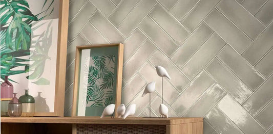 Estudio Cerámico Vermont 'Greige', beige-grijze glanzende wandtegels in visgraatverband achter een houten dressoir met vazen