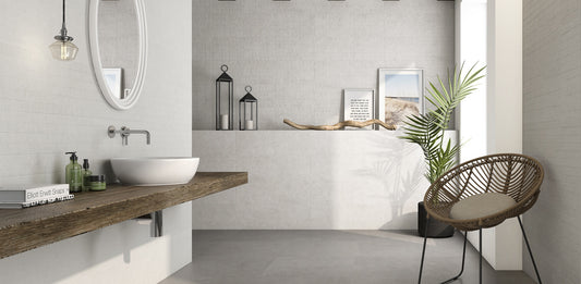 Argenta Cerámica Wave 'Resin Snow', crèmekleurige betonlook wandtegels in een badkamer met wastafelblad, spiegel en stoel