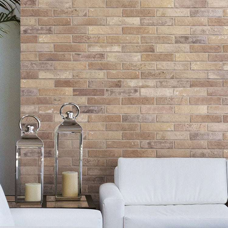 Beige baksteenlook wandtegels in halfsteensverband achter een witte bank met twee zilveren kaarsenlantaarns