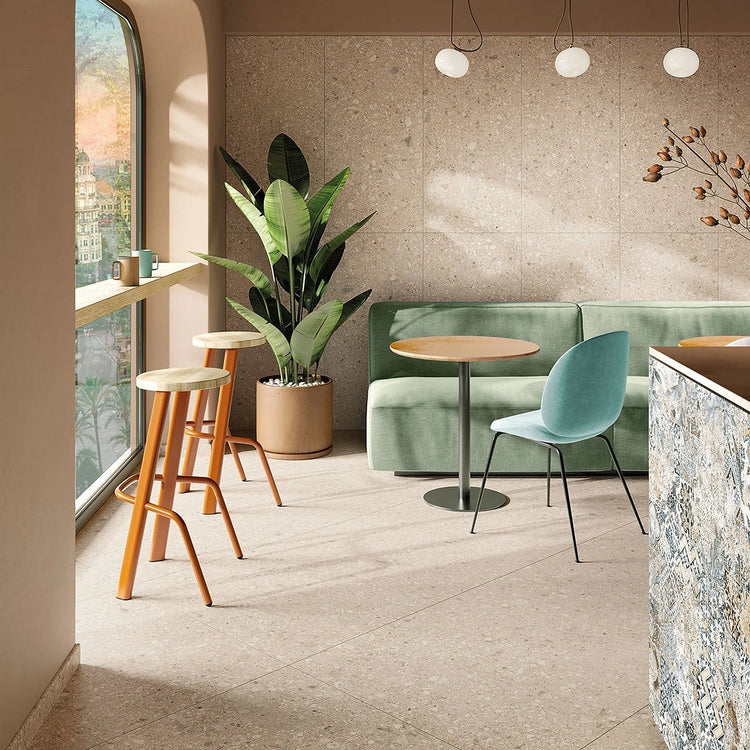 Beige tegels in een lichte ruimte met boogvenster, planten en groene zitmeubels