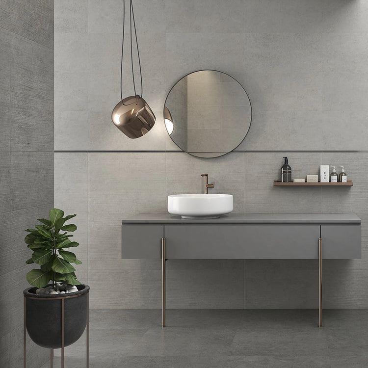 Grijze betonlook wandtegels in een badkamer met wastafel en vrijstaand bad