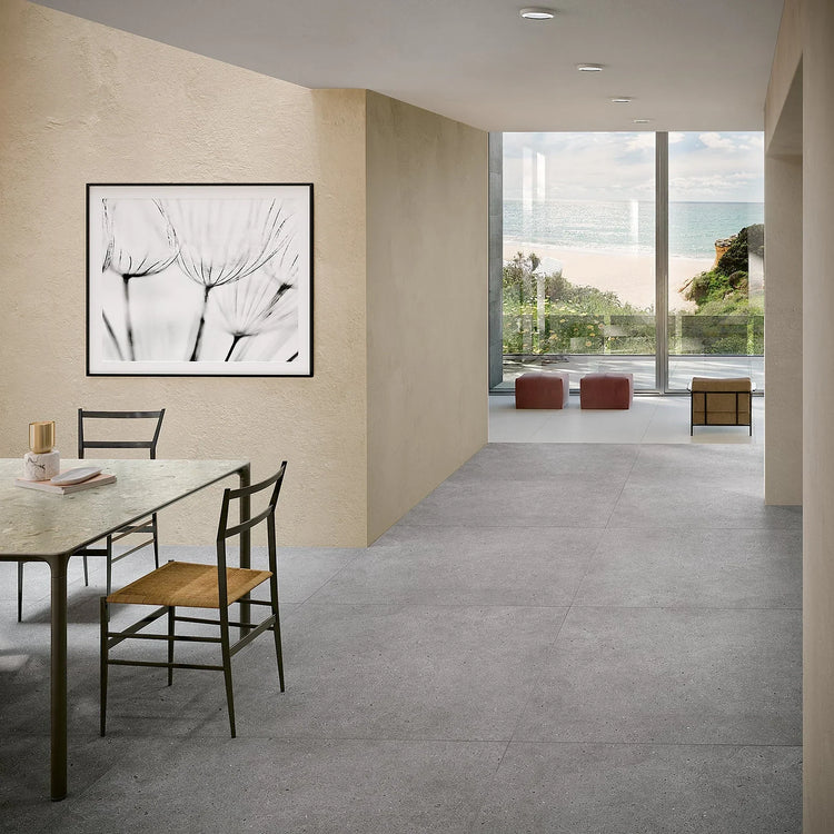 EnergieKer Brera, grijze betonlook vloertegels in een eetkamer met doorkijk naar een zithoek met zeezicht