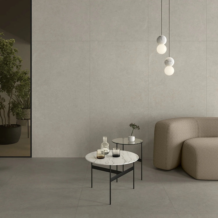 Lea Ceramiche Intense, grijze vloertegels en beige-grijze wandtegels in een lounge met ronde bank en marmeren bijzettafels
