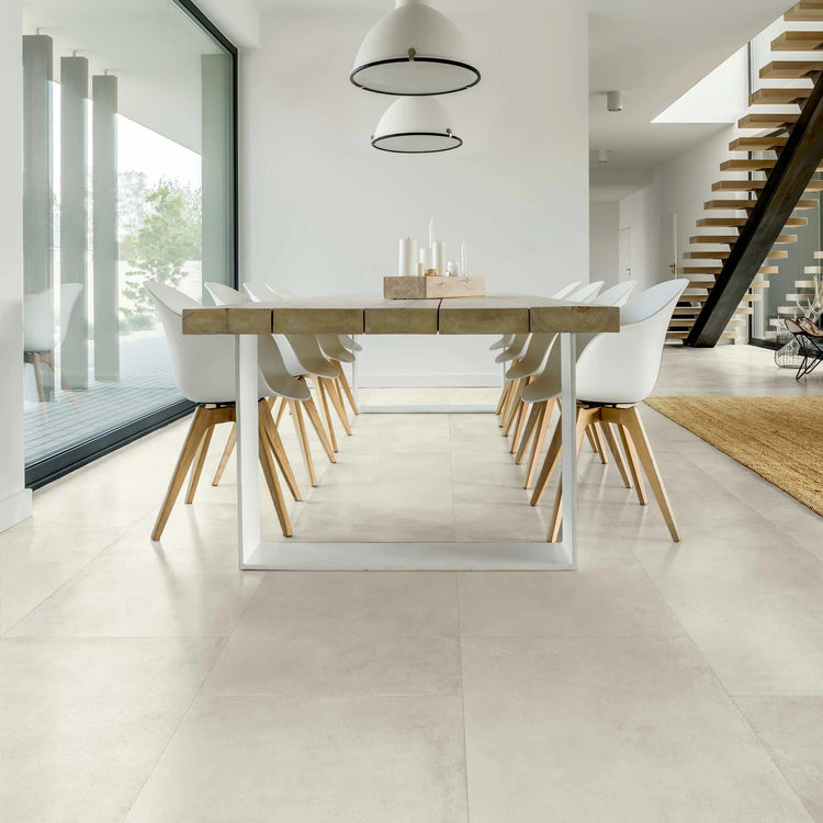 Lichte matte betonlook vloertegels in een eetkamer met lange houten tafel en witte stoelen