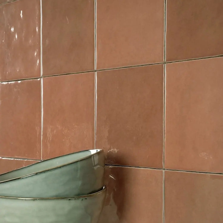 Oranje glanzende wandtegels met een zachte terracottatint, met twee gestapelde zeegroene schalen ervoor