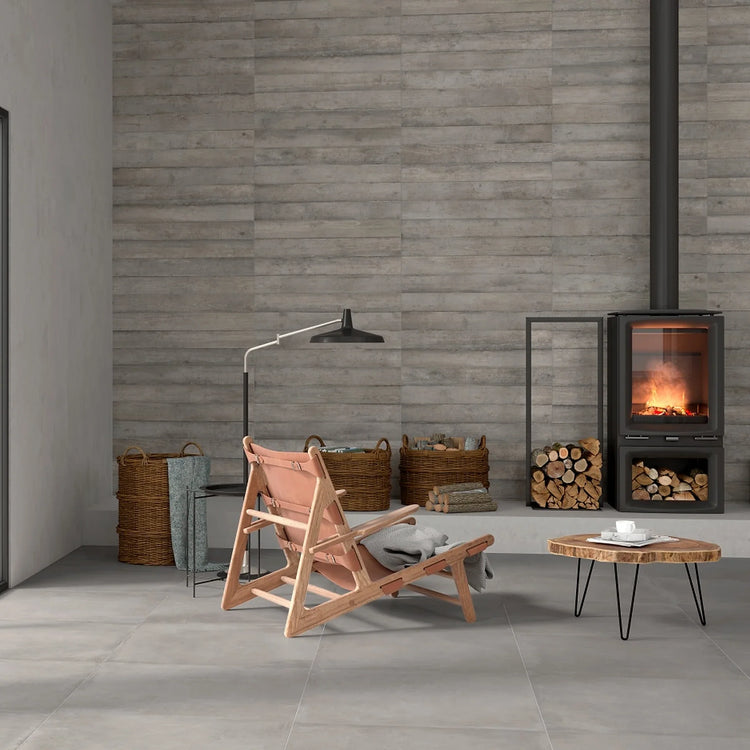 Argenta Cerámica Powder 'Argent', beige-grijze betonlook vloertegels bij een houtkachel, loungestoel en boomstamtafel