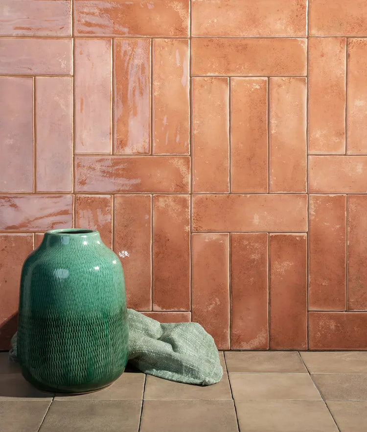 Roze glanzende wandtegels met warme terracotta-nuances, met een zeegroene vaas ervoor