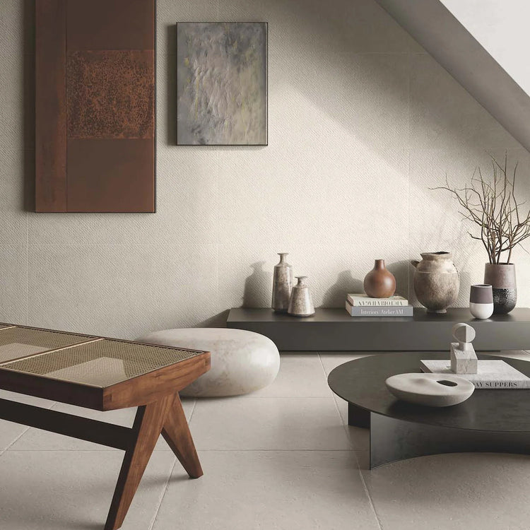 Casalgrande Padana Stile, crème vloer- en wandtegels in een lichte woonkamer met houten bank, lage tafels en keramiek