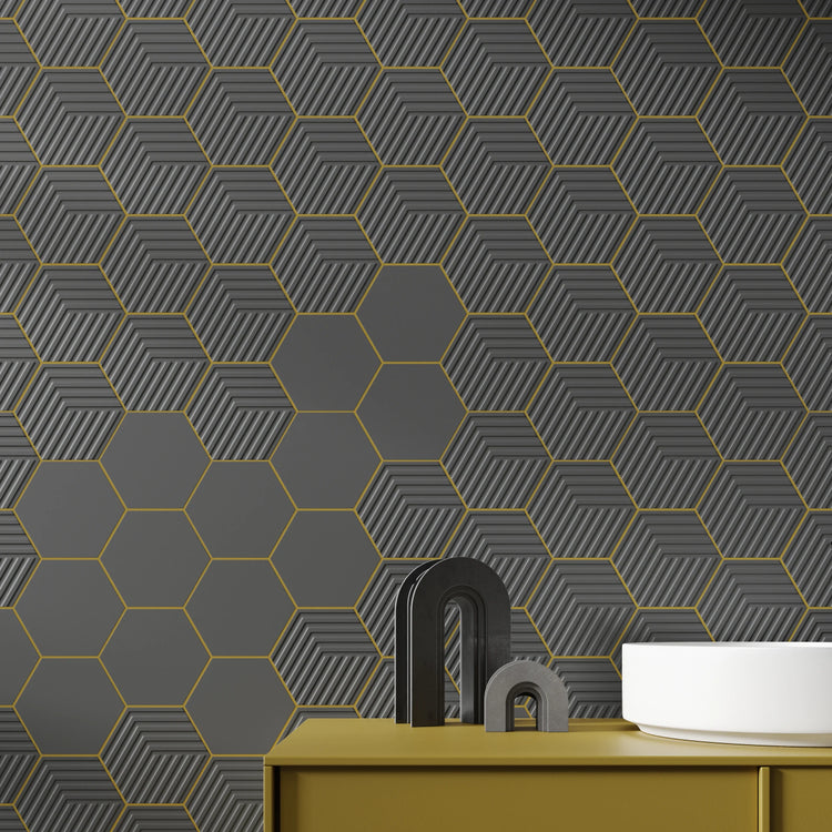Donkergrijze hexagon wandtegels, effen en met streeprelief, met goudkleurige voegen boven een okergeel badmeubel
