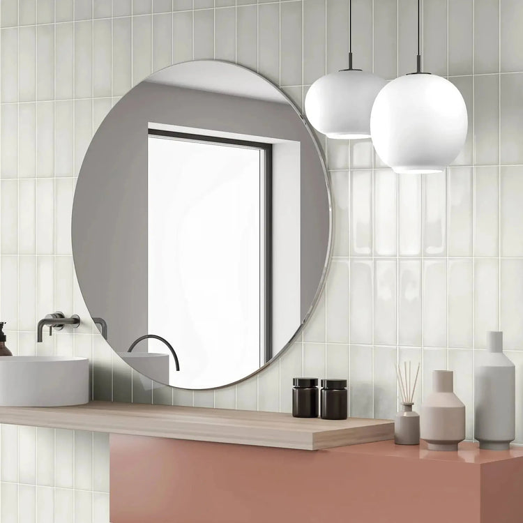 Witte geribbelde wandtegels in een badkamer met ronde spiegel en roze wastafelmeubel