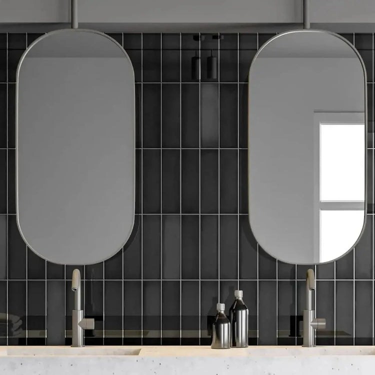 Zwarte geribbelde wandtegels in een badkamer met twee ovale spiegels en dubbele wastafel