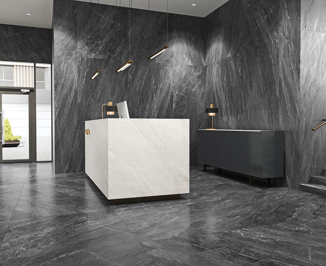 EnergieKer Agathòs 'Anthracite', antracieten natuursteenlook tegels op wand en vloer in een ontvangstruimte met witte balie