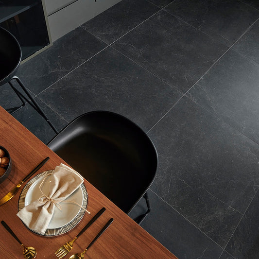 Keraben Bleuemix 'Black Soft', antracieten vloertegels van bovenaf met een eettafel, gedekt bord en een zwarte schaalstoel