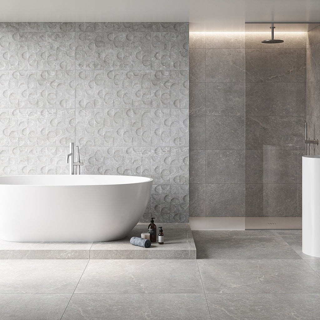 Keraben Bleuemix 'Grey Soft', lichtgrijze vloertegels in een badkamer met vrijstaand bad, een reliëfwand en een inloopdouche