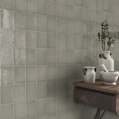 Estudio Cerámico Borriana, grijsbeige glanzende wandtegels in een hoek met een houten wandtafel en keramieken kruiken