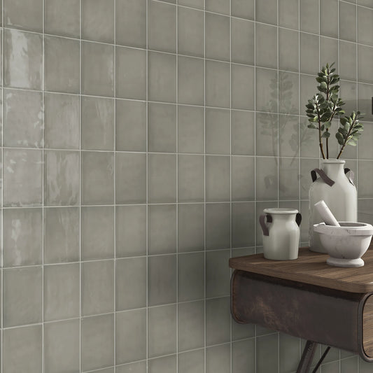 Estudio Cerámico Borriana, grijsbeige glanzende wandtegels in een hoek met een houten wandtafel en keramieken kruiken