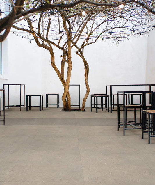 EnergieKer Brera 'Bloom', beige-grijze betonlook vloertegels op een terras met een boom, statafels en een lichtsnoer