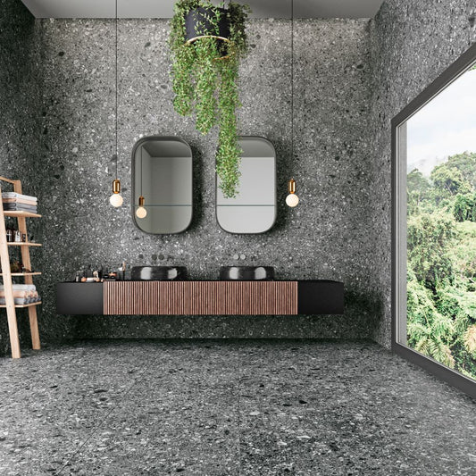 Tuscania Ceppo di Gré 'Anthracite', donkergrijze terrazzo tegels in een badkamer met twee ovale spiegels en een hangplant