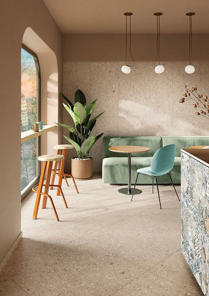 Tuscania Ceppo di Gré 'Beige', beige terrazzo vloer- en wandtegels in een koffiebar met groene bank en witte bollampen