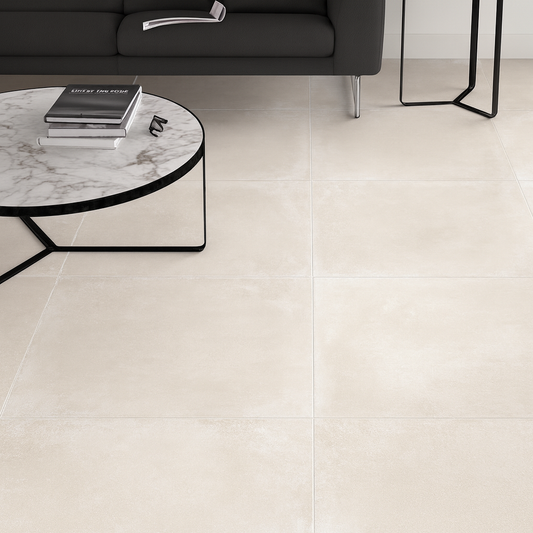 Cerpa Cerámica Concrete 'Perla', crèmekleurige betonlook vloertegels in een woonkamer met donkere bank en marmeren salontafel