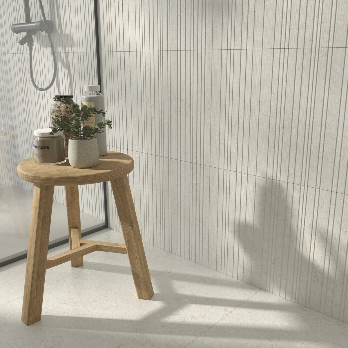 Cifre Cronos 'Ivory Laja', reliëfwand in een douche met houten krukje, planten en ivoorwitte vloer