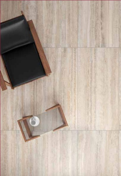 Tuscania Dolomia Stone 'Almond Vein', lichte travertijnlook vloertegels met een zwarte leren fauteuil en glazen bijzettafel