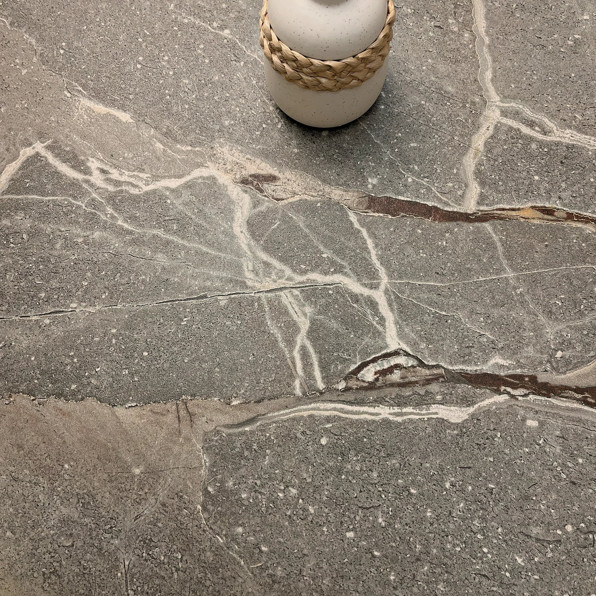 La Platera Dusk 'Taupe', detail van taupe marmerlook tegel, hier 60x60cm, met witte aders en een vaas