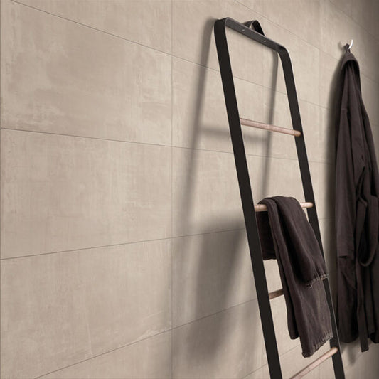 Ceramica Valsecchia Galaxy 'Beige', beige betonlook wandtegels met een zwarte handdoekladder en donkere badjas ervoor
