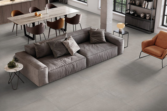 Ceramica Valsecchia Galaxy 'Grey', lichtgrijze betonlook vloertegels van bovenaf met grote grijze bank en cognac fauteuil
