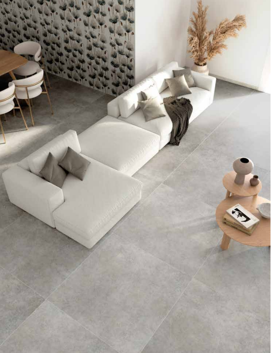 Tuscania Grey Soul 'Mid', grijze betonlook vloertegels van bovenaf in een woonkamer met witte loungebank en reliëfwand