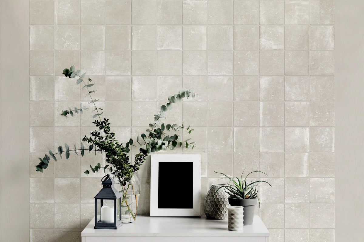 Savoia Italia Heritage 'Sand', crèmekleurige vierkante wandtegels achter een witte console met lantaarn en eucalyptus
