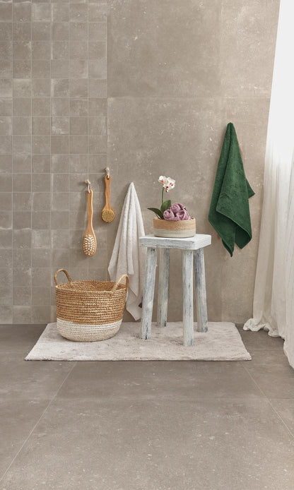 Savoia Italia Heritage 'Taupe', taupe wandtegels en grote vloertegels in een badkamer met rieten mand, kruk en orchidee