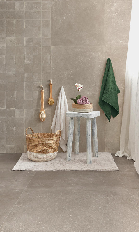 Savoia Italia Heritage 'Taupe', taupe wandtegels en grote vloertegels in een badkamer met rieten mand, kruk en orchidee