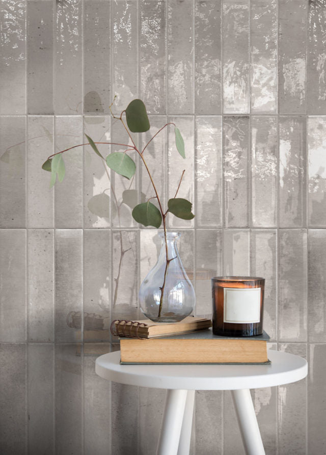 Keradom Home 'Ash', grijze glanzende Brick wandtegels achter een bijzettafel met een eucalyptustak en een kaars