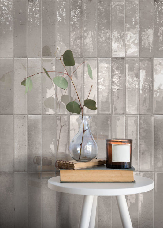 Keradom Home 'Ash', grijze glanzende Brick wandtegels achter een bijzettafel met een eucalyptustak en een kaars