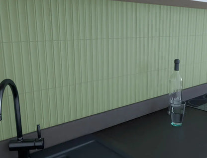 Estudio Cerámico Jaipur 'Celadon', lichtgroene geribbelde wandtegels als keukenachterwand met zwarte kraan en glazen fles