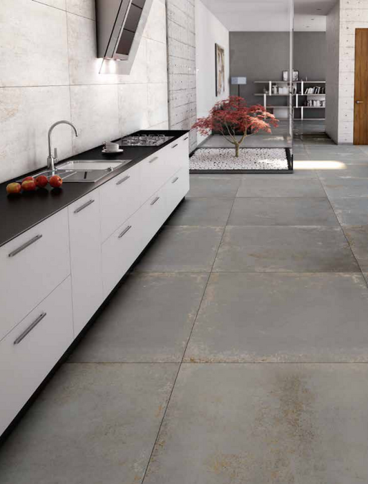 Tuscania Metropolitan 'Nichel', grijze betonlook vloertegels in een keuken die doorlopen naar een binnentuin met esdoorn