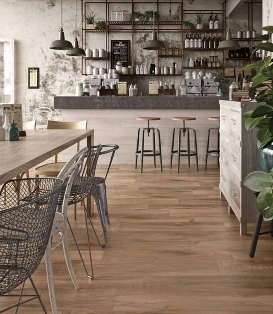 Tuscania North Wind 'Brown', bruine houtlook vloertegels in een industrieel café met betonlook wanden en metalen draadstoelen