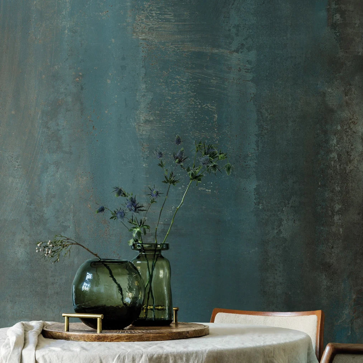 EnergieKer Oxidatio 'Cuprum', groene metaallook wand met oxidatievlekken achter een ronde tafel met glazen vazen en distels