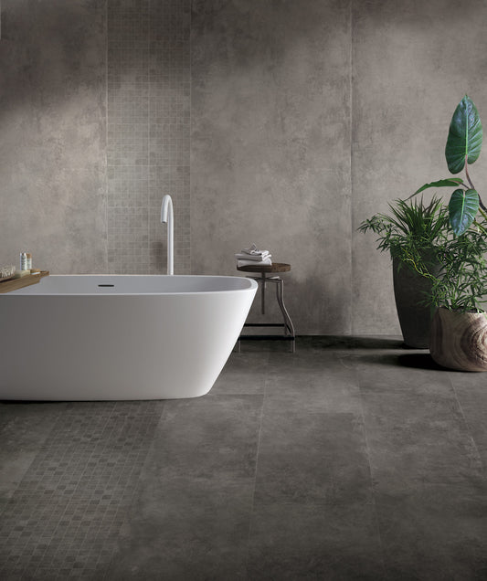 EnergieKer Parker 'Anthracite', donkergrijze betonlook wand- en vloertegels in een badkamer met vrijstaand wit bad en plant