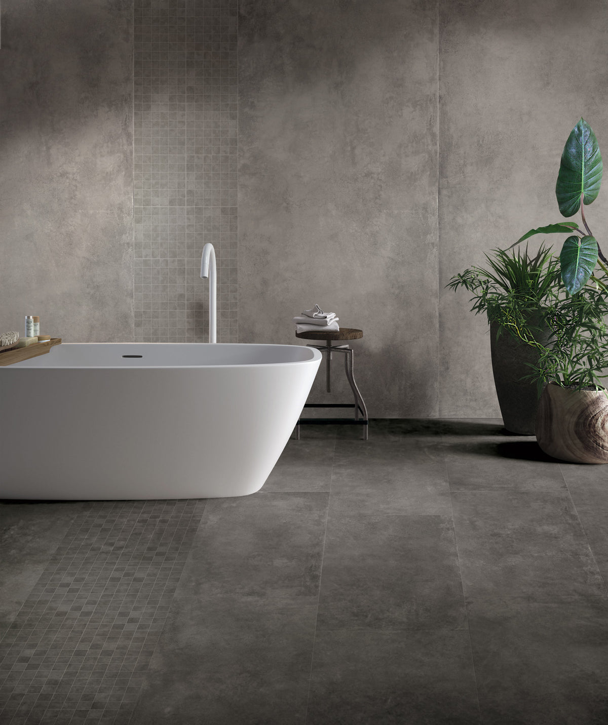 EnergieKer Parker 'Anthracite', donkergrijze betonlook wand- en vloertegels in een badkamer met vrijstaand wit bad en plant