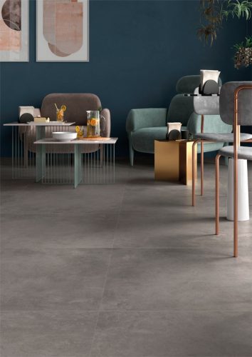 Ceramica Valsecchia Recover 'Dark', grijze betonlook vloertegels in een loungehoek met donkerblauwe wand en lage fauteuils